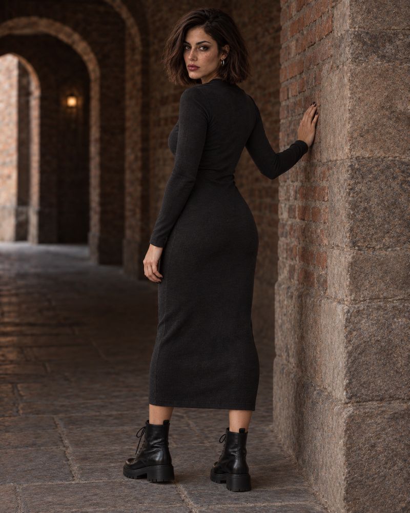 Sabine in a black dress looking back over her shoulder beneath brick arches at dusk.
